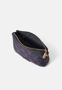 Černá prošívaná kabelka s kultivovaným zlatým zipem, otevřená, aby odhalila černý interiér. Má elegantní design a boční popruh pro nošení.