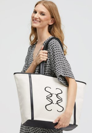 Canvas tote bag in cream with black leather accents, featuring an embroidered abstract design. Structured shape with dual handles.