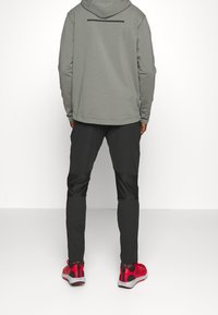 Grå huvtröja med långa ärmar, tillsammans med svarta byxor med texturerade paneler och röda sportskor med grå accenter.