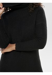 Maglione collo alto nero con un design a maglia testurizzato, caratterizzato da maniche lunghe e una vestibilità morbida, mostrato piegato al collo.