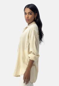 Camicia panna morbida e texturizzata, con colletto, abbottonatura e maniche arrotolate, realizzata in un tessuto leggero e traspirante.