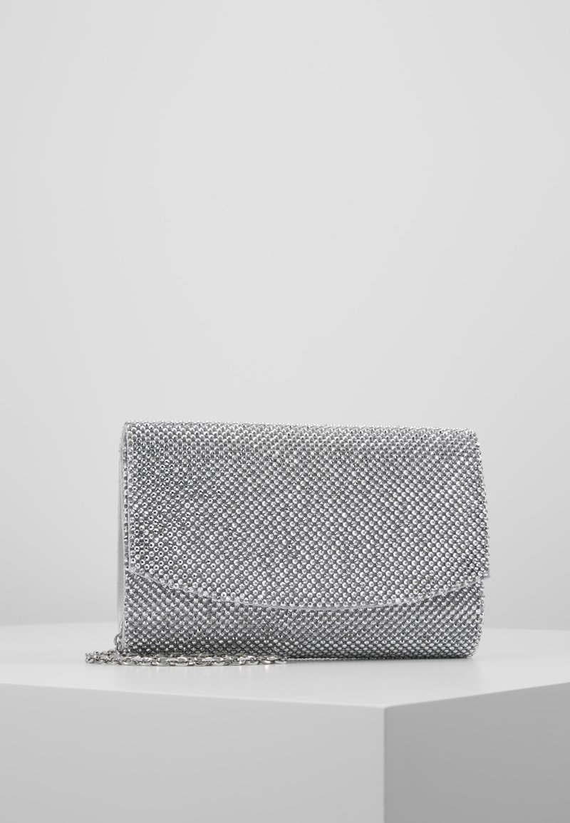 Pochette recouverte de strass argentés avec fermeture à rabat et petite bandoulière en chaîne, posée sur une surface blanche devant un fond uni.