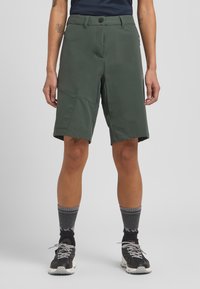 Grüne Shorts aus leichtem Material, mit geradem Schnitt, vorderen Taschen und einer Reißverschlusstasche an der Seite.