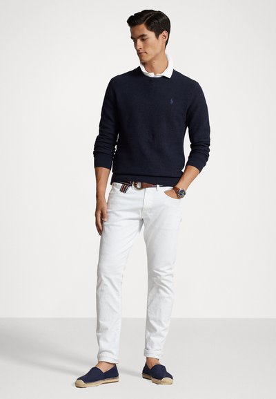 Suéter azul-marinho, camisa de colarinho branca por baixo, calças brancas e espadrilhas azuis-marinho. Apresenta um corte ajustado e costura detalhada no suéter.