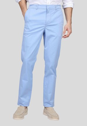 Pantalons en coton bleu clair avec une coupe ajustée, des poches latérales et des passants de ceinture, associés à des chaussures beige à enfiler.