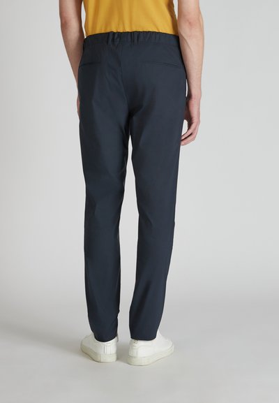 Granatowe spodnie elastyczne w pasie z bocznymi kieszeniami, zwężanym krojem i gładką fakturą. Noszone z białymi sneakerami, prezentując minimalistyczny design.