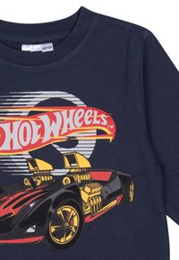 Maglietta a maniche lunghe di colore blu navy con una grafica vivace di una macchina Hot Wheels, arricchita da accenti rossi, gialli e neri, che mette in evidenza un design elegante e dettagli audaci.