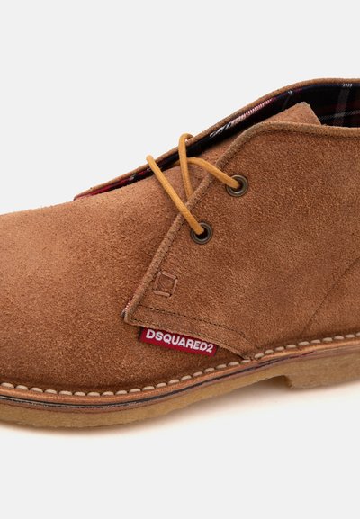 Chaussure en daim marron à lacets couleur beige, doublure intérieure à carreaux, semelle blanche cousue et étiquette rouge marquée DSQUARED2.