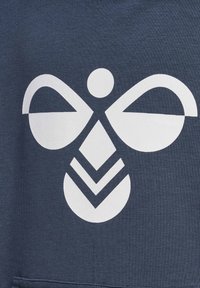 Design geometrico astratto che ricorda un'ape stilizzata con ali, cerchi e chevron bianchi su uno sfondo di tessuto scuro.