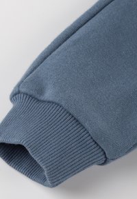 Heller blauer Baumwollpulloverbund mit geripptem Textur und glattem Stoff, versehen mit einer gestickten Naht an der Oberkante für zusätzliche Details.