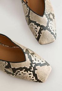 Kärjetön korkokenkä, jossa on tekstuuri-snaikkinäyttö beige ja musta. Sileä sisävuori ja kiiltävä pinta ulkopuolella.