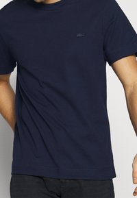 Navy blue cotton t-shirt with short sleeves, crew neck, and a subtle embroidered logo on the chest. Smooth texture and casual design.