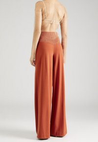 Naken mesh långärmad topp med texturerat mönster och vida rostfärgade byxor med slät yta och avslappnad passform.