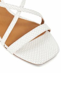 Witte platte sandaal met kruisbanden, voorzien van een gestructureerd slangenleerpatroon, vierkante neusvorm en een bruine binnenzool.