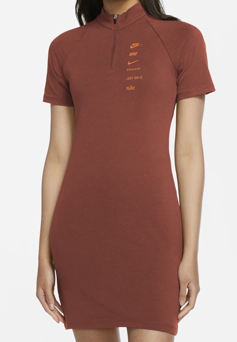 Czerwona bawełniana sukienka z wysokim kołnierzem, krótkimi rękawami i zamkiem błyskawicznym do jednej czwartej. Na froncie znajduje się pomarańczowe logo Nike oraz napisy. Gładka tekstura.