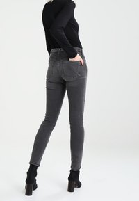 Úzké šedé džíny s vybledlým vzhledem, pěti kapsami a detaily šití. Nosené s černým topem a vysokými podpatky.