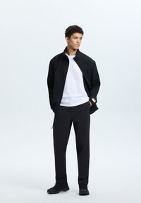 Black lightweight jacket with a high collar, paired with a white T-shirt and black pants. Textured fabric and zippered pockets visible.