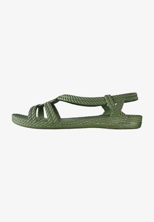 Green sandals made of textured material, featuring a braided strap design, open toe, and a flat sole with a woven appearance.