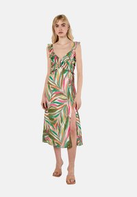 Robe maxi florale avec imprimé de feuilles vertes, roses et blanches, décolleté en V profond, bretelles froncées et fente sur le côté. Texture du tissu douce.
