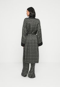 Mustast ja hallist mustriga hommikumantel vöökohas vööga ja lahtiste varrukatega, millel on geomeetriline kujundus sileda kanga peal, stiilitud sobivate pükstega.