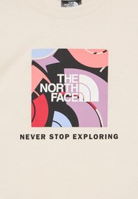 Το λογότυπο της The North Face σε λευκό χρώμα πάνω σε πολύχρωμο αφηρημένο τετράγωνο με το κείμενο «Μην σταματάς ποτέ να εξερευνάς» από κάτω σε μπεζ ύφασμα.