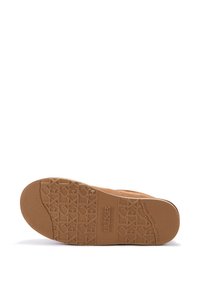 Tan suede boot with a textured rubber sole, featuring a patterned grip and embossed logos, designed for comfort and durability.