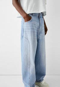 Světle modré, volně střižené džíny s viditelným vyblednutím, bočními kapsami a neutrálním odstínem. Nosí se s bílým zkráceným tričkem a světlou obuví.