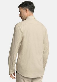 Camisa de manga larga beige, hecha de tela texturizada, con un cuello clásico y puños abotonados, con un dobladillo ligeramente curvado y un ajuste relajado.