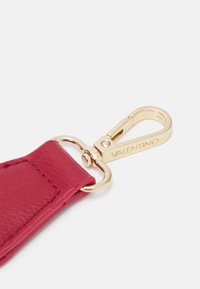 Růžový kožený přívěšek na klíče se zlatým kovovým klipem a kroužkem. Obsahuje viditelné vyryté jméno značky na sponě a hladký povrch.