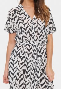 Sukienka w czarno-białe wzory z krótkimi rękawami, kołnierzykiem i przewiązaną talią. Wykonana z lekkiej, teksturowanej tkaniny.
