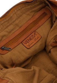 Hnědý textilní interiér tašky s kapsou na zip a koženým štítkem označeným "VENEZIA Originální kůže." Hladká textura, jednoduchý design.