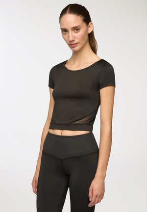 Top sportivo nero corto con maniche corte, caratterizzato da un'inserto in rete trasparente e una texture liscia, abbinato a leggings neri a vita alta.