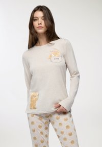 Maglia a maniche lunghe color beige chiaro con illustrazioni di orsi e la scritta "Love"; abbinata a pantaloni da pigiama beige a fantasia con orsi.