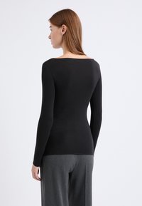 Langärmliges, schwarzes Oberteil mit einem Boot-Ausschnitt, figurbetonter Silhouette und glatter Textur, kombiniert mit grauen, locker sitzenden Hosen.