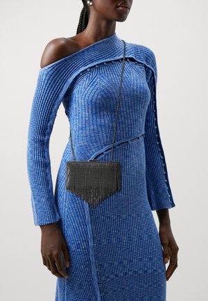 Mujer con un vestido azul de un solo hombro con textura acanalada, detalles de botones y un pequeño bolso negro con correa de cadena cruzado al torso.