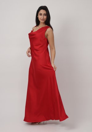 Kvinde iført en gulvlængde rød satin kjole med ét skulderærme, der poserer mod en ensfarvet lys baggrund.
