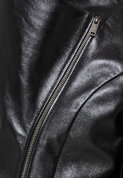 Gros plan sur une veste en cuir noire brillante avec une fermeture éclair diagonale en argent partiellement fermée.