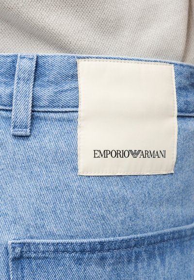 Κοντινή λήψη της μέσης παντελονιού από ανοιχτό μπλε τζιν με λευκή ετικέτα Emporio Armani ραμμένη πάνω από την πίσω τσέπη.