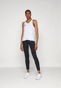 White athletic tank top with black accents, paired with black leggings and white athletic shoes. Slim fit and smooth fabric.
