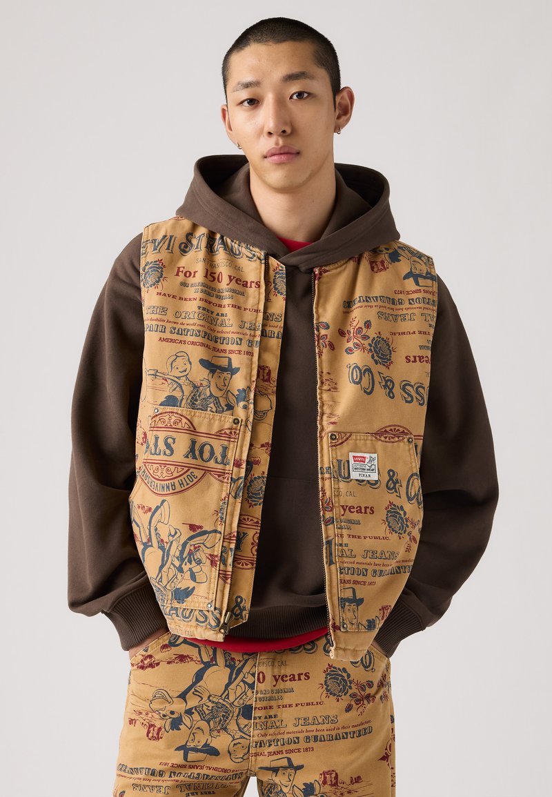 Brun hoodie under en beige vest med farverige trykte grafik, der har vintage-inspirerede illustrationer og tekst. Bemærkelsesværdig Levi's lap detalje.