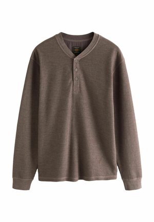 Brun bomull långärmad henley-tröja med ribbat mönster, tre-knappars knappslå och rund halsringning. Ärmslut och fåll är ribbade.