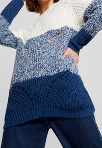 Chunky stickad tröja med färgblockdesign i vitt, ljusblått och mörkblått, med öppet vävda detaljer och ribbade muddar.