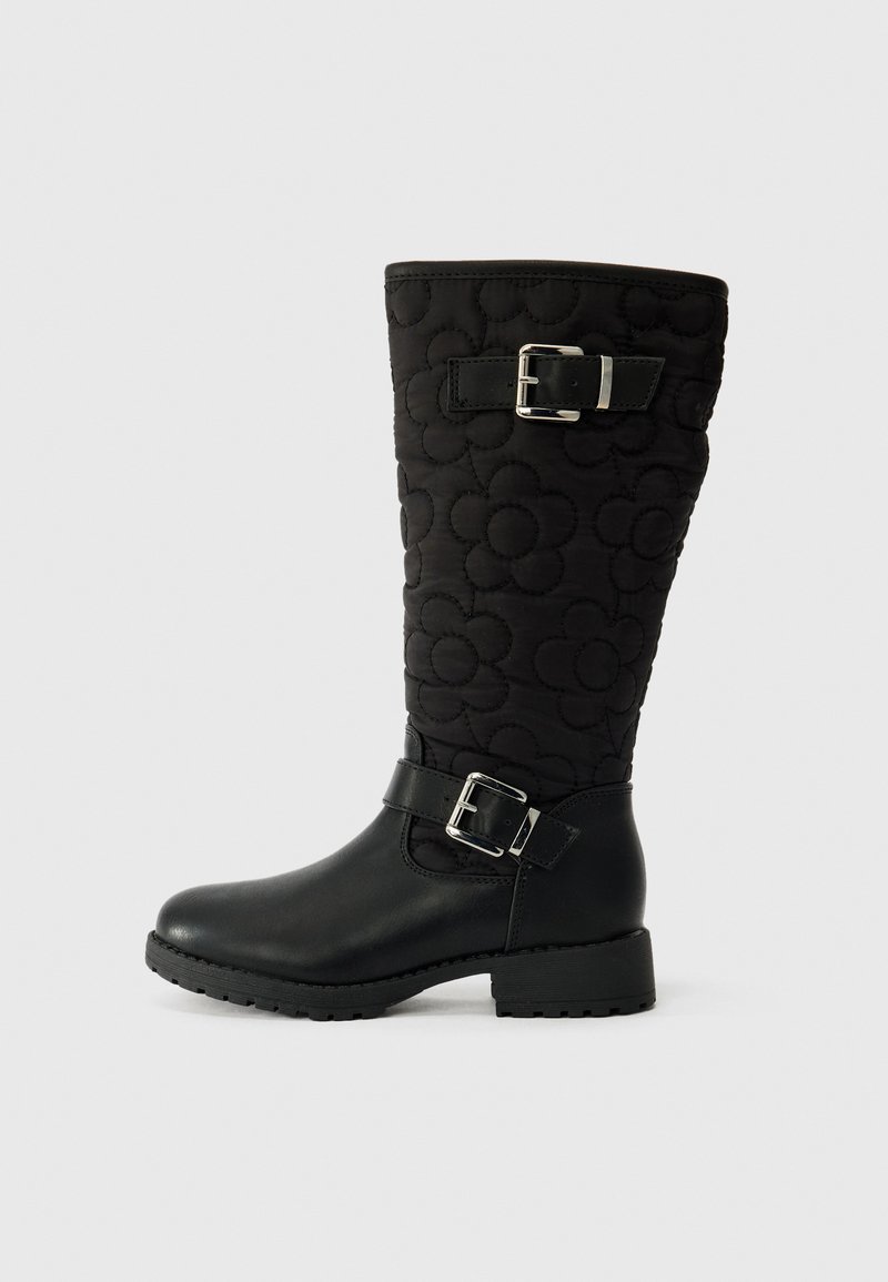 Botas negras hasta la rodilla con parte superior de tela acolchada con patrones de flores, sección inferior de cuero y hebillas metálicas decorativas.