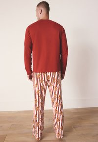 Rode blouse met lange mouwen gecombineerd met witte broek met een rood en goud patroon van peperkoekmannetjes tegen verticale strepen.