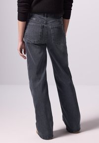 Wijdvallende jeans van donkergrijs denim, met een hoge taille en twee achterzakken. De stof heeft een zachte textuur met subtiele vervagingdetails.