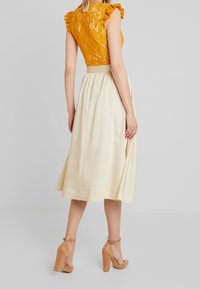 Gul spetsliv med volangärm parat med en krämfärgad kjol i knälängd. Bruna ankelremssandaler fulländar looken.