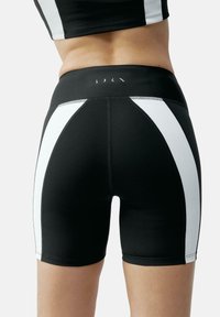 Črne atletske hlače s belimi stranskimi paneli, ki imajo gladko teksturo, elastičen pas in podrobnosti z kontrastnim šivom.