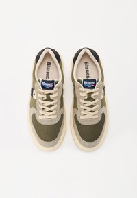 Grønne og beige joggesko med overdel i mesh og semsket lær, beige snøring, svart hælakkent og en merkebølge på tunga.