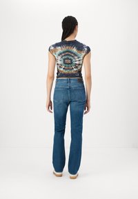 Kratki tie-dye crop top s kratkim rukavima u tamnim bojama, te flared traperice s srednjim strukom i pet džepova.