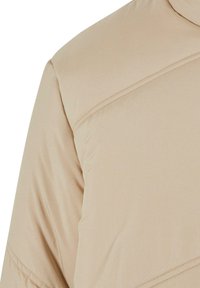 Beige dunjakke med høy krage, subtil quiltet tekstur og skråsting over brystet for ekstra designdetalj.